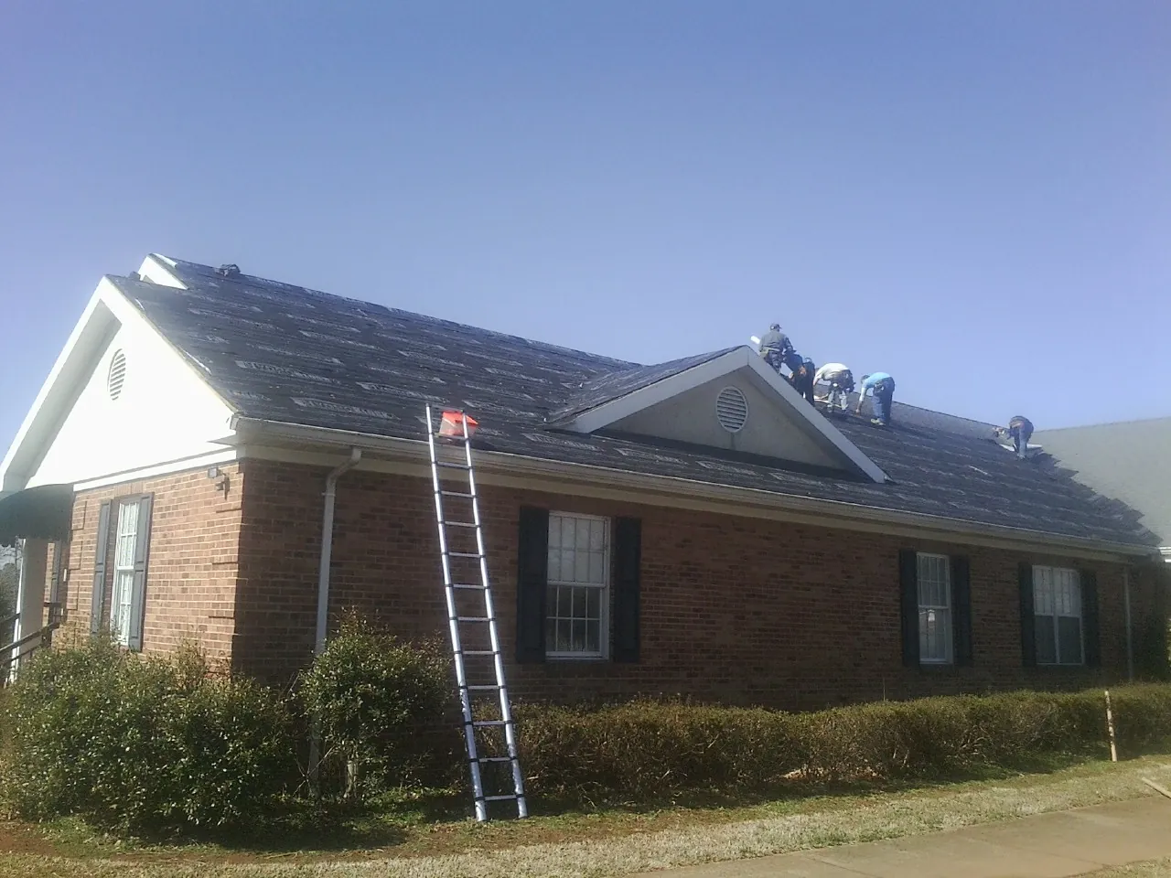 Crew tearing shingles off a brick ranch roof with a ladder set — Metal Roof Repair work by our crew in Midway